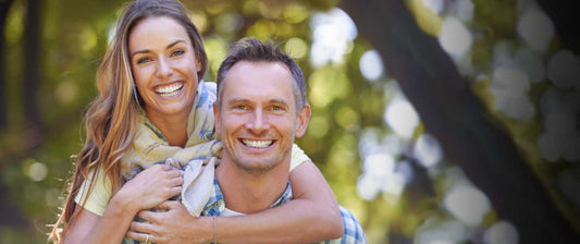 A smiling couple holding each other from behind, with the man in a plaid shirt and the woman in a colorful top.